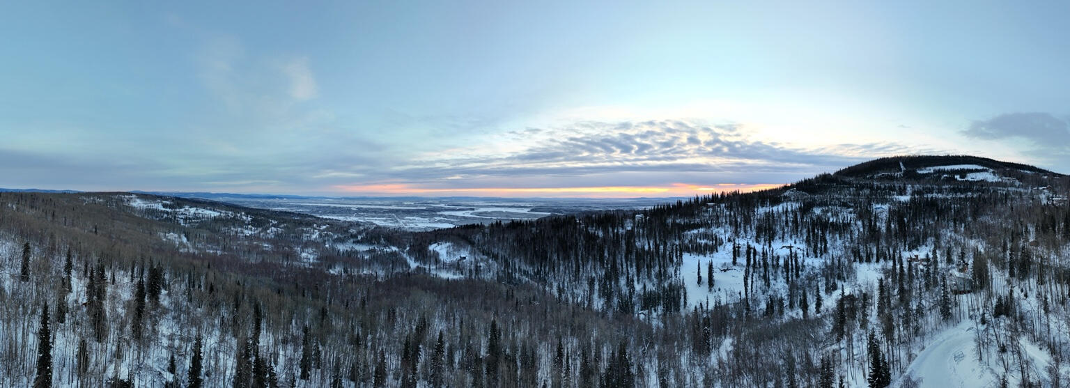 Panoramic view of snowy wooded hills opening into a broad valley beneath a cloudy sky.